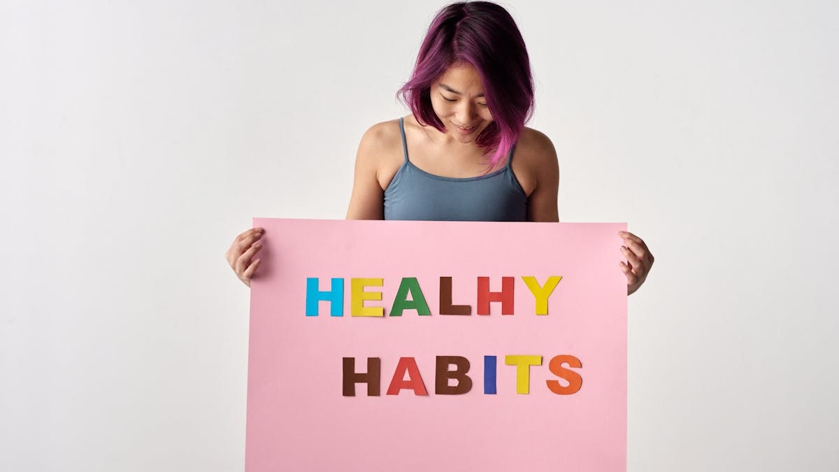 Asian woman holding a colorful 'Healthy Habits' sign in a studio setting, promoting wellness.
